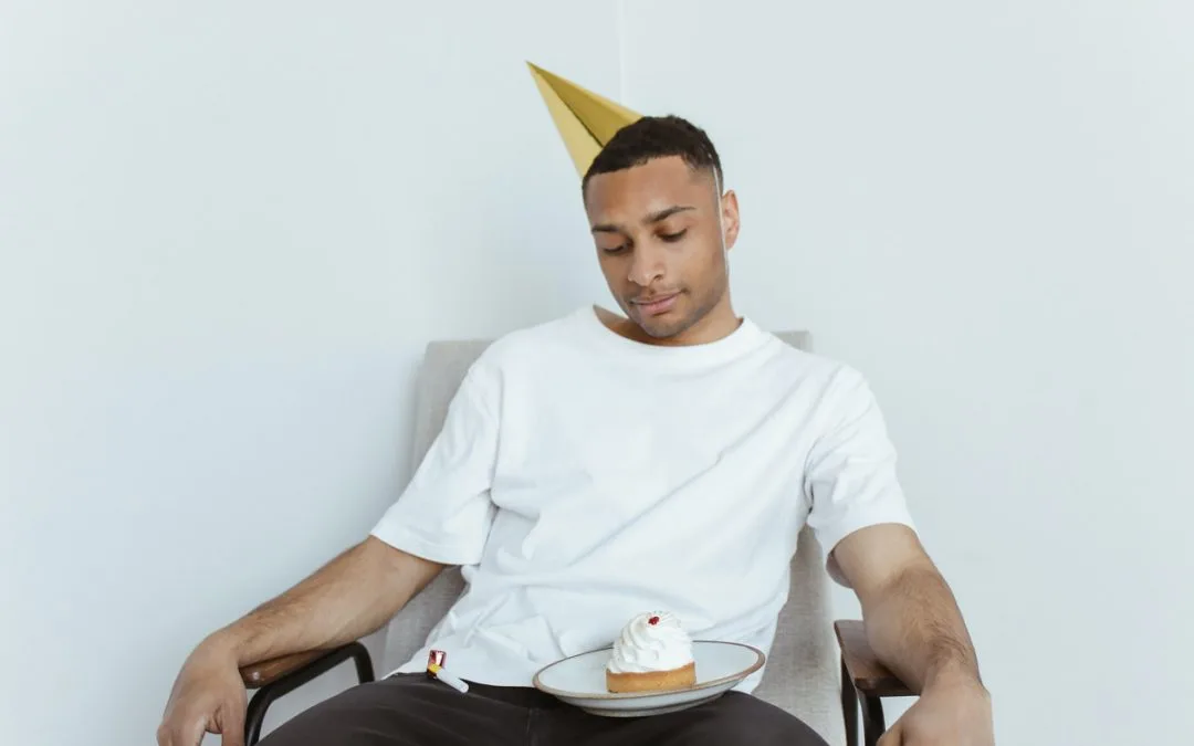 A sad young man with a party hat and a cupcake